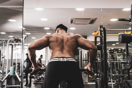 Muscular men exercising with weights. He is performing T bar rows for back muscle / Bodybuilder in the gym