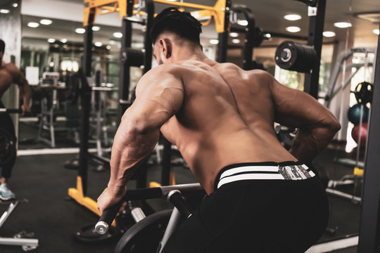 Muscular men exercising with weights. He is performing T bar rows for back muscle / Bodybuilder in the gym