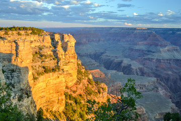 Cloudy sky with sun illuminating a cliff - Grand Canyon National Park South Rim. Warn yellow tones and blue cold tones.