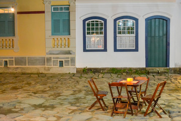 White and yellow old colonial houses entrances with a wodden table and four chairs in front of them - Paraty`s Historical City (Rio de Janeiro, Brazil)