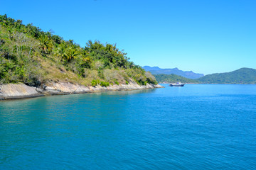 Island`s coast bathed Blue sea with a small boat in Paraty`s Island (Rio de Janeiro - Brazil). Green and blue tones