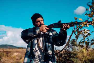 Bearded hunter man holding gun and walking in forest. Hunter with shotgun gun on hunt. Big game.