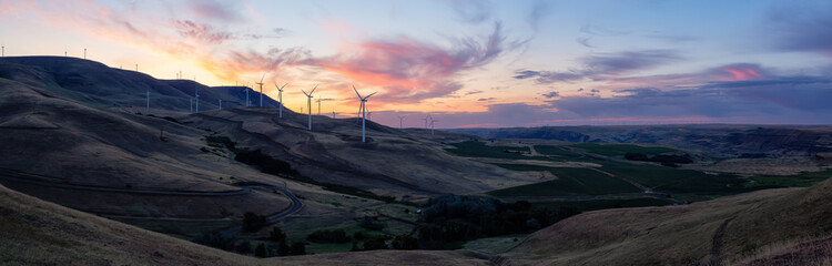 Beautiful Panoramic Landscape View of Wind Turbines on a Windy Hill during a colorful sunrise....