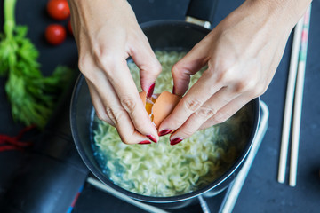 Young woman cracks egg into the boiled noodle