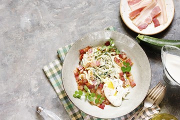 Low-Carb keto carbonara pasta with spaghetti (noodles) of zucchini with cream, fried bacon and poached egg. decorated with pea sprouts. in a beautiful light dish. top view.  copy space