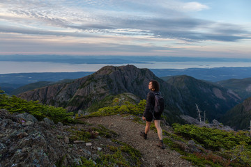 Naklejka na ściany i meble Adventurous girl hiking the beautiful trail in the Canadian Mountain Landscape during a vibrant summer sunset. Taken at Mt Arrowsmith, near Nanaimo, Vancouver Island, BC, Canada.