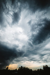 Dramatic cloudscape. Sunny light through dark heavy thunderstorm clouds before rain. Overcast rainy bad weather. Storm warning. Natural gray background of cumulonimbus. Sunlight in stormy cloudy sky.