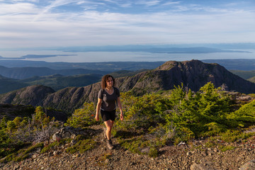 Naklejka premium Adventurous girl hiking the beautiful trail in the Canadian Mountain Landscape during a vibrant summer evening. Taken at Mt Arrowsmith, near Nanaimo, Vancouver Island, BC, Canada.