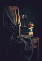 Still life. Old vintage chair with a bottle of wine and a glass, pink flower protea and books on a dark background. Postcard. Free space for your text.