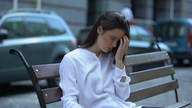 Exhausted woman sitting on bench, suffering from migraine pain, health problem