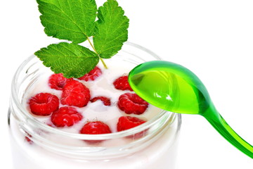 Pink cream or milk fruit yogurt with natural ripe red raspberry berry and green raspberry leaves in open glass transparent jar and curved slim graceful spoon on white background close up. Isolated