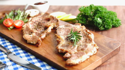 Close up grilled pork chop steak topped with Fresh rosemary herb on wooden plate