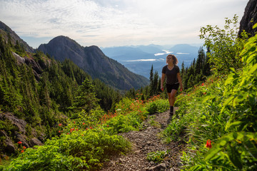 Fototapeta premium Adventurous girl hiking the beautiful trail in the Canadian Mountain Landscape during a vibrant summer evening. Taken at Mt Arrowsmith, near Nanaimo, Vancouver Island, BC, Canada.