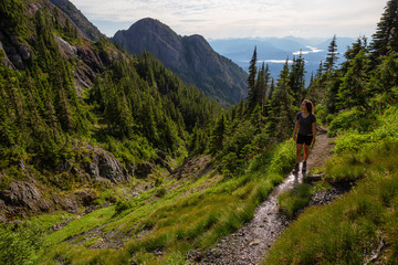 Fototapeta na wymiar Adventurous girl hiking the beautiful trail in the Canadian Mountain Landscape during a vibrant summer evening. Taken at Mt Arrowsmith, near Nanaimo, Vancouver Island, BC, Canada.