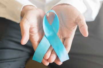 Light blue ribbon awareness on hand of business male for Men's Health and National Prostate Cancer Awareness Month in November