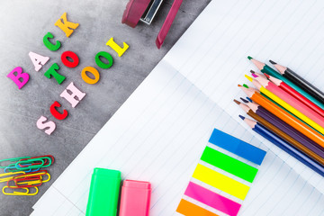 The layout of school supplies on a dark gray background. Top view, the sun's rays from the side. Flat lay. Back to school.
