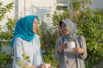 portrait of two hijab  women drinking tea in front of the house and talking