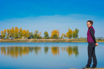 Fototapeta na wymiar Beautiful young woman enjoying autumn by the side of a wild lake