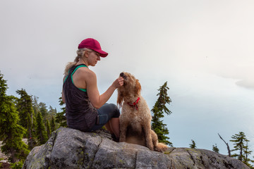 Adventurous Girl is hiking with a dog on top of Unnecessary Mountain during a sunny and cloudy summer day. Located in West Vancouver, British Columbia, Canada.