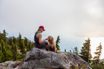 Adventurous Girl is hiking with a dog on top of Unnecessary Mountain during a sunny and cloudy...