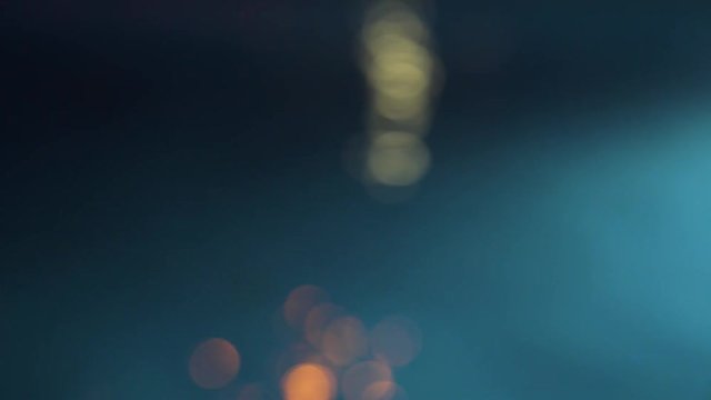Light reflected off a swimming pool at night using an out of focus lens creating a bokeh effect of moving balls of light. The shot is then slowly re focused until the surface of the water is clear.