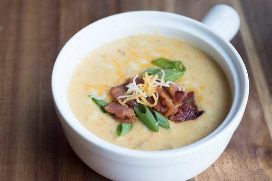 Warm soup with bacon, green onions and shredded cheese on a wooden background