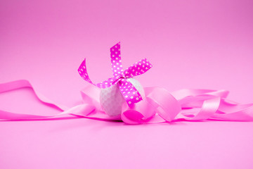 Golf ball with pink ribbon is on pink background