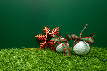 Golf ball with Christmas ribbon and snow flake are on green grass.