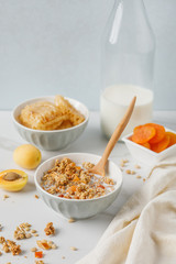 Bowl of granola with dried apricot on white table. Wooden spoon.