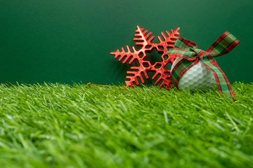 Golf ball with Christmas ribbon on green grass