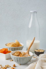 Bowl of granola with dried apricot on white table. Wooden spoon.