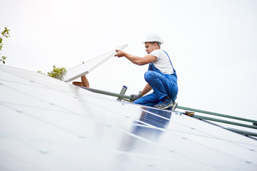 Construction worker connects photo voltaic panel to solar system using screwdriver. Professional installing and construction of solar system, alternative energy and financial investment concept.