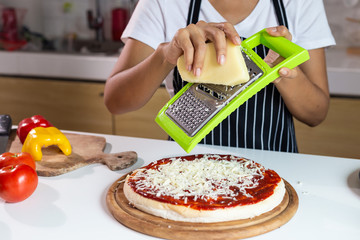 Woman sprinkle cheese on the pizza
