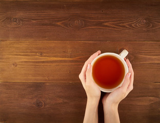 Woman holding a cup of tea on dark wooden background top view copy space