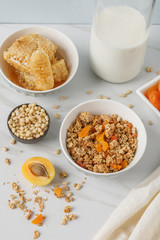 Bowl of granola with dried apricot on white table. Wooden spoon.