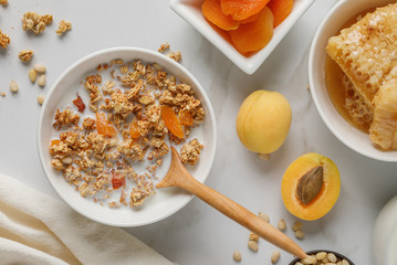 Bowl of granola with dried apricot on white table. Wooden spoon.