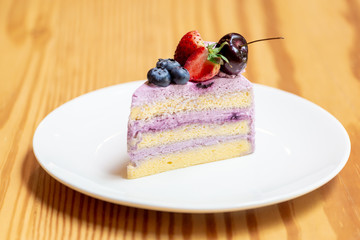 Blueberry Raspberry Cake with Strawberries and cherries topping  on wooden table in coffee cafe