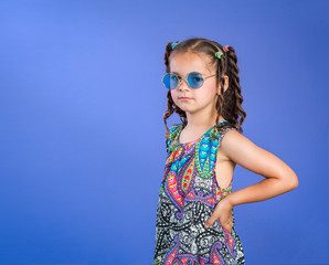 Serious face little girl in hippie sunglasses and paisley flowered shirt isolated on blue background