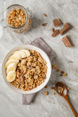 Breakfast with granola with banana. Pieces of chocolate and jar of granola on background.