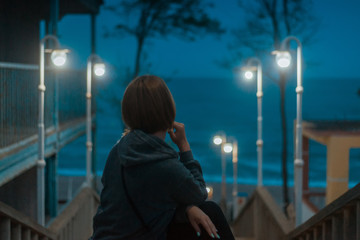 Woman in the light of street lamps on the alley overlooking the sea coast.