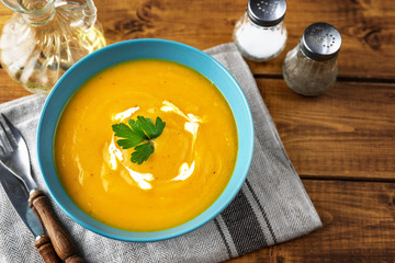 Pumpkin soup with cream in blue plate and parsley on dark wooden background