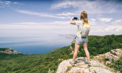Naklejka premium Young woman hiker with backpack standing on a cliff
