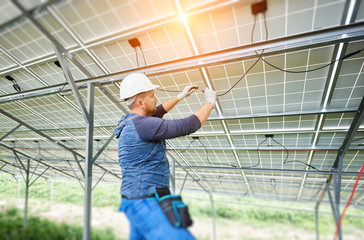 Young electrician connecting electrical cables inside the lit by sun solar modules. Installing and...