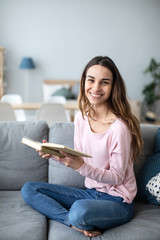 Obraz premium Young woman sitting on sofa at home and reading a book.