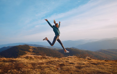 woman jumping on mountain on sunset sky and mountains background