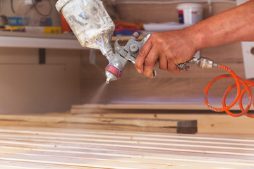 A man covers wooden boards with varnish in the workshop with a spray.