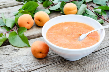 Apricot jam in a white bowl and ripe apricots on a wooden table.