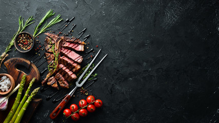 Fototapeta na wymiar Beef T-Bone steak on a black table. Top view. Free space for text.