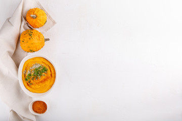 Spicy pumpkin soup served with pumpkin seeds and parsley.  Bowl with autumn squash soup on white table. Top view. Copy space.