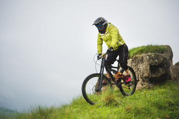 Fototapeta na wymiar Aged male athlete in helmet and mask rides down a grassy slope on a mountain bike. Downhill mountain bike concept